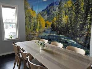 A dining area with a table, chairs, a window, and a mural of a river and forest.