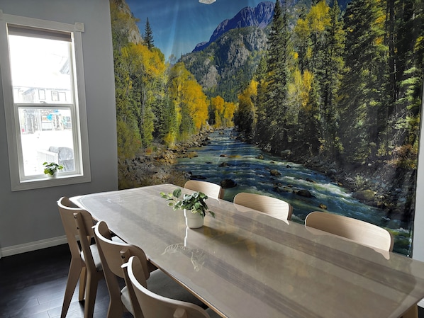 A dining area with a table, chairs, a window, and a mural of a river and forest.