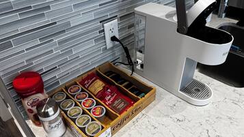 Una encimera de cocina con una cafetera, un tazón de azúcar y una caja de cápsulas de café.