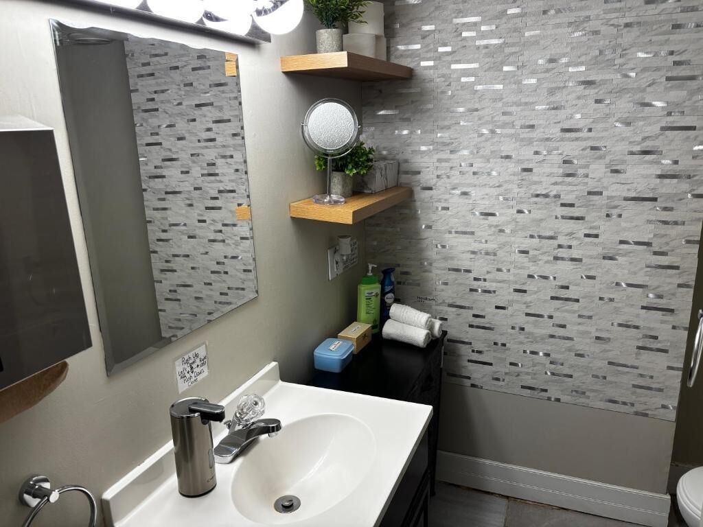A bathroom with a white sink, a mirror, a towel rack, and a shower area.