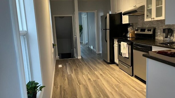 Una cocina moderna con suelo de madera, electrodomésticos de acero inoxidable y armarios blancos.