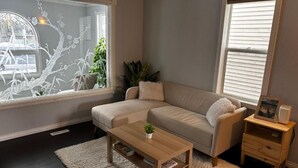 Una sala de estar con un sofá, una mesa de centro, un tapete, una mesita auxiliar con un marco de fotos y una ventana con persianas.