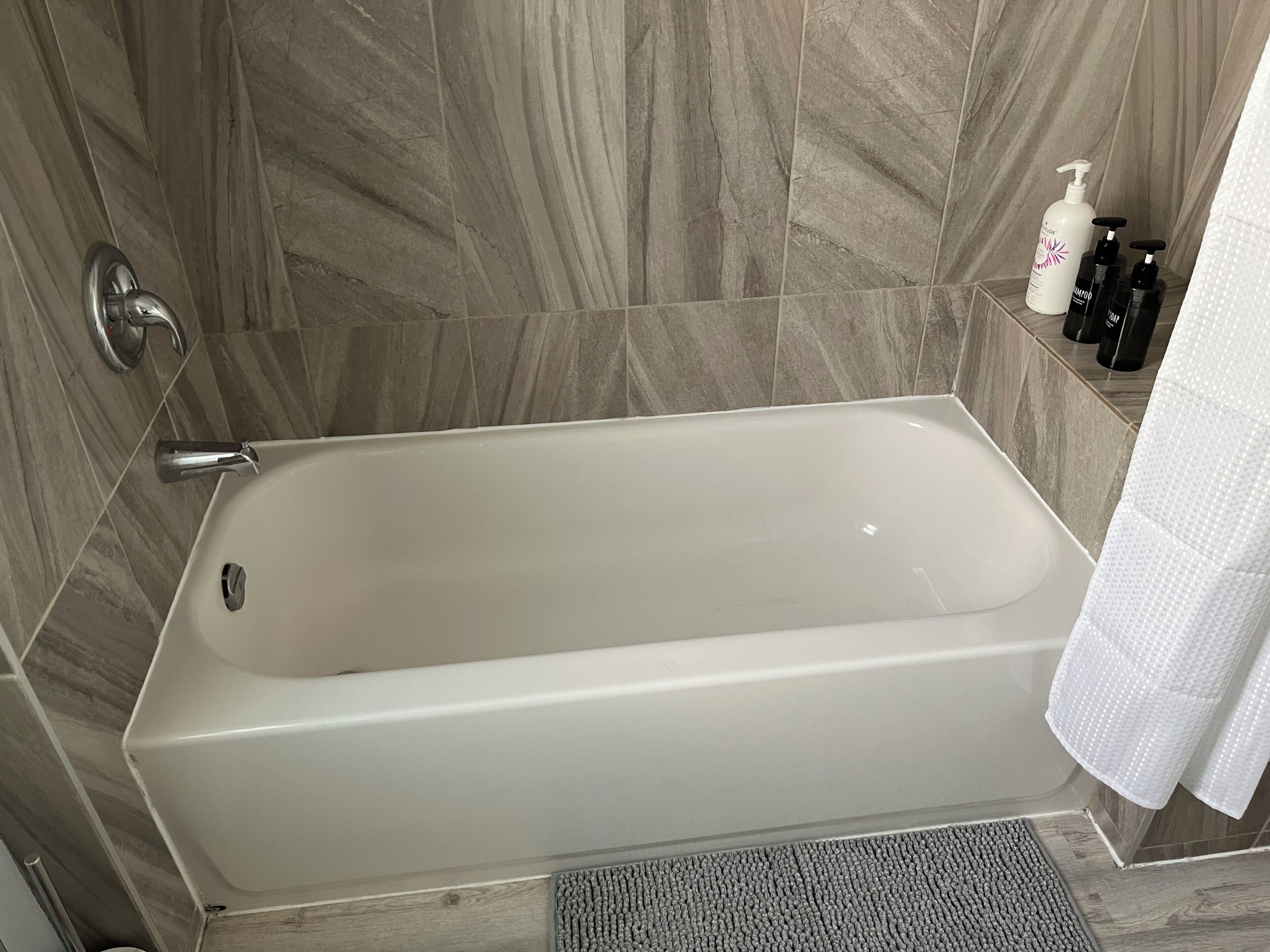 A modern bathroom with a bathtub, a shower, and a toilet. There are toiletries on a shelf.