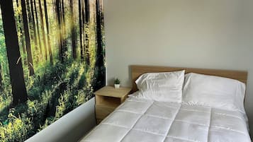 A bedroom with a bed, a nightstand, a small potted plant, and a forest-themed wall mural.