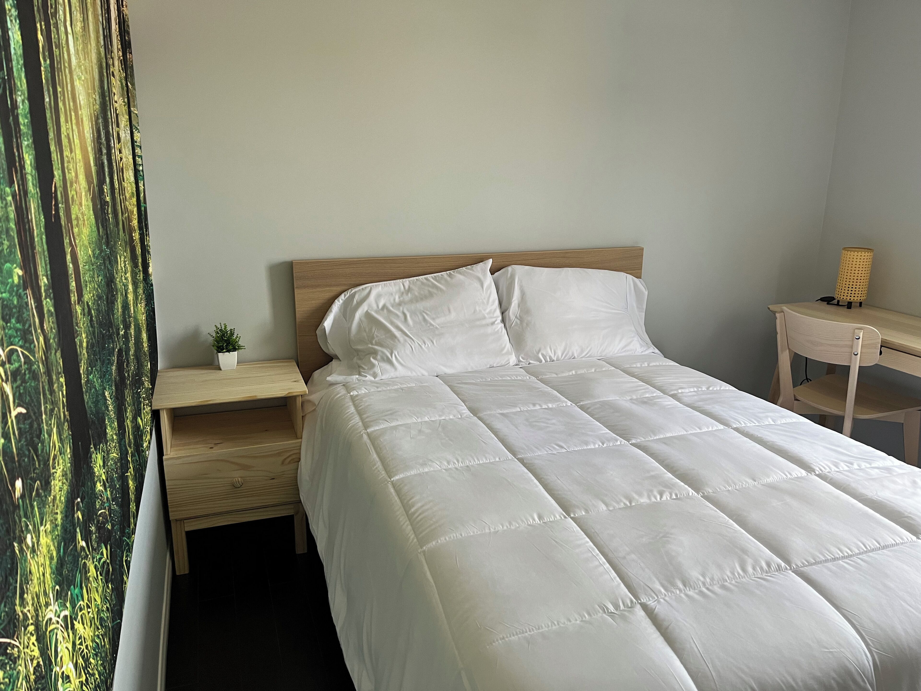 Een bed met een houten hoofdbord, een nachtkastje met een lamp en een kleine plant.