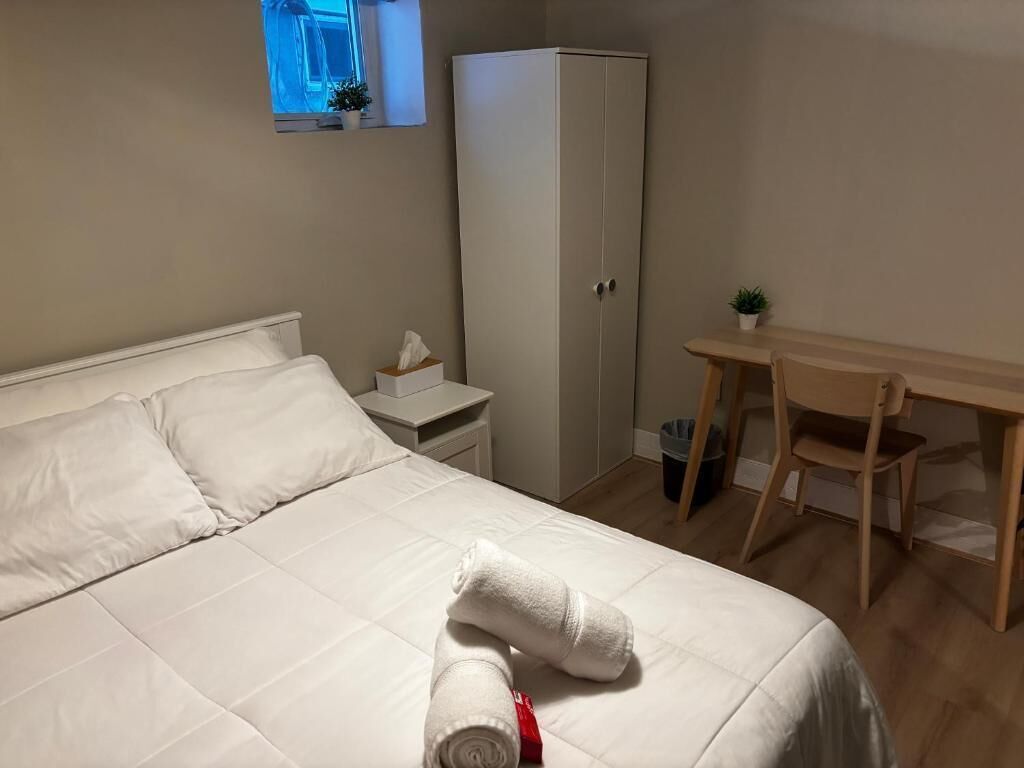 A bedroom with a bed, a desk, a wardrobe, and a small window.