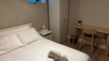 A bedroom with a bed, a desk, a wardrobe, and a small window.