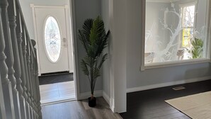 Un pasillo con una escalera, una planta en maceta, un ventanal con vistas a un árbol y una puerta que da a otra habitación.