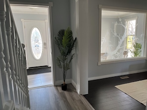 A hallway with a staircase, a potted plant, a large window with a tree view, and a door leading to another room.