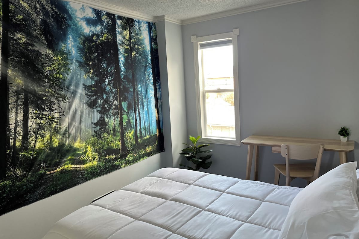Un dormitorio con cama, escritorio, silla, ventana y un adorno de pared con motivos forestales.