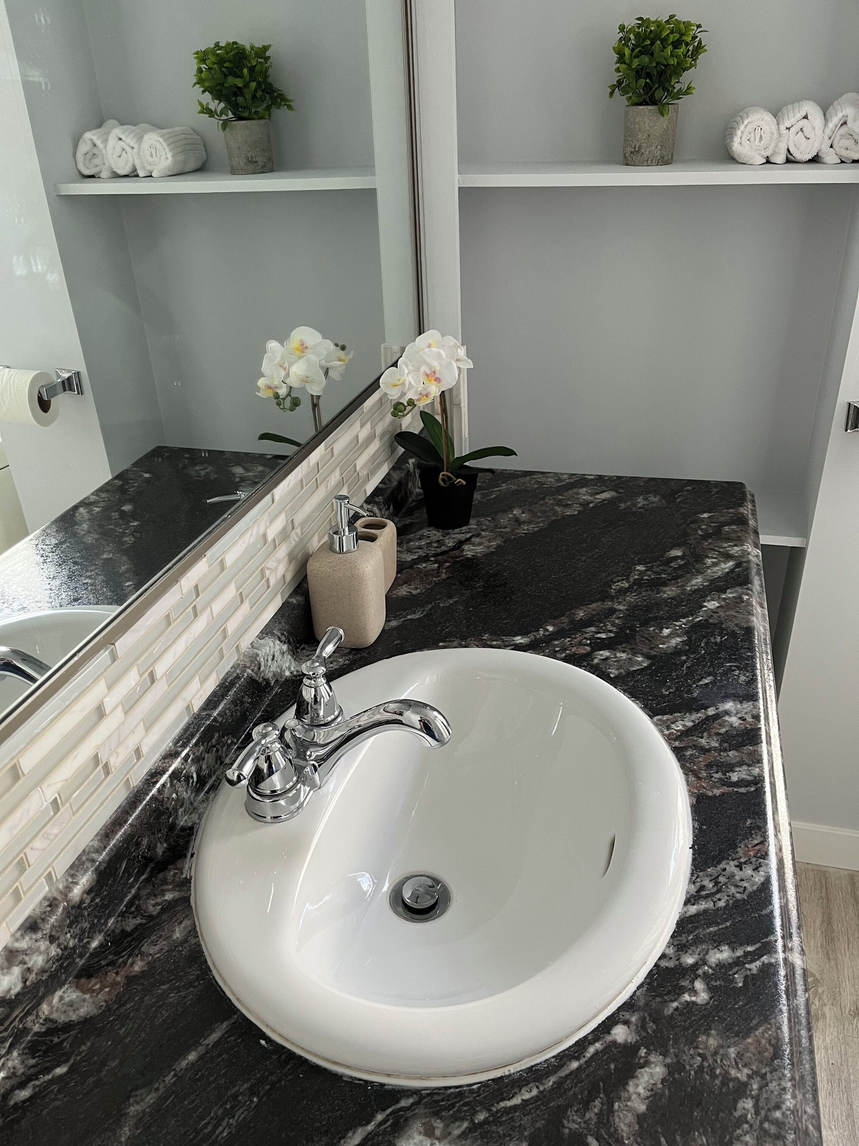 Un baño con lavamanos blanco, encimera de mármol y espejo.