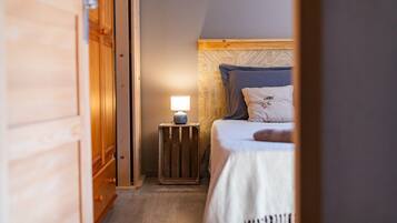 Un couloir étroit mène à une chambre à coucher qui contient un lit, une table de chevet avec une lampe et une armoire en bois.