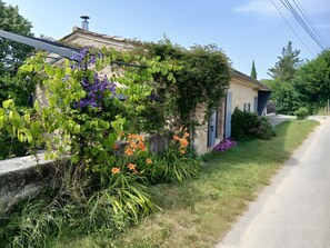 Una casa rustica con un muro in pietra, un tetto in metallo e un giardino pieno di piante e fiori.