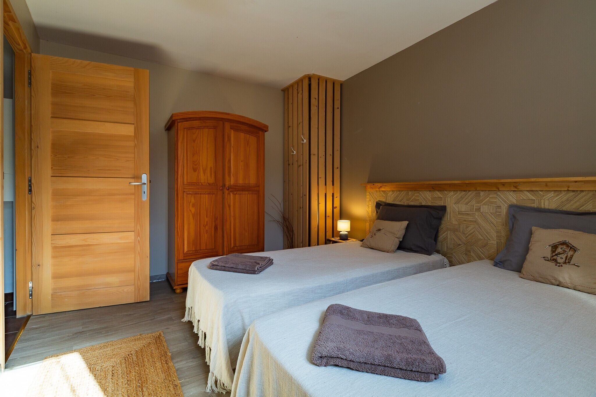 Une chambre avec deux lits, une armoire en bois et une table de chevet avec une lampe.