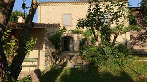Un edificio in pietra rustico con un piccolo ingresso, una panchina verde e un albero sullo sfondo.