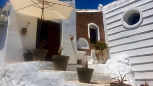 Um edifício branco com uma janela redonda, plantas em vasos e um grande guarda-sol.