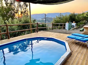 Eine Holzterrasse mit Swimmingpool, Liegestühlen und Blick auf die Landschaft.