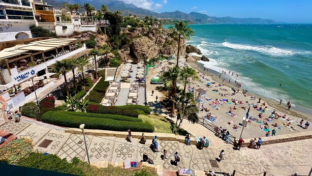 A beachside hotel with outdoor seating, palm trees, and a view of the ocean.