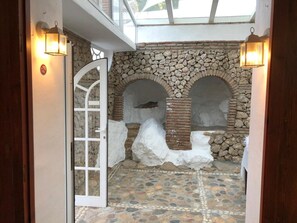 Un pasillo con paredes de piedra, suelo de baldosas, una puerta de cristal y dos luces empotradas.