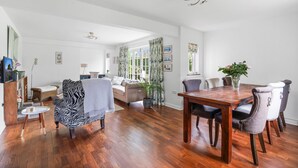 A spacious living room with a wooden dining table, a zebra-patterned armchair, and a sofa. - Dairy Close Parking By My Getaways (Uckfield)