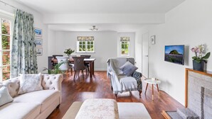 A living room with a sofa, armchair, dining table, chairs, and a fireplace. - Dairy Close Parking By My Getaways (Uckfield)