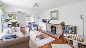 A living room with a sofa, ottoman, fireplace, bookshelf, and chessboard. - Dairy Close Parking By My Getaways (Uckfield)