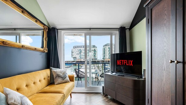 A modern living room with a sofa, a TV, and a view of a balcony with buildings. - Marina Haven Sea Views Parking By My Getaways (Brighton)