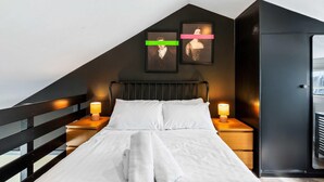 A bedroom with a sloped ceiling, a bed with white linens, two bedside lamps, and two framed pictures on the wall. - Marina Haven Sea Views Parking By My Getaways (Brighton)