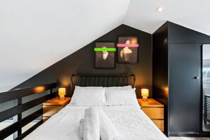 A bedroom with a sloped ceiling, a bed with white linens, two bedside lamps, and two framed pictures on the wall. - Marina Haven Sea Views Parking By My Getaways (Brighton)