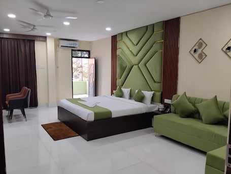 A modern hotel room with a large bed, a green sofa, a brown armchair, and a ceiling fan.. The Pride Gitbitan