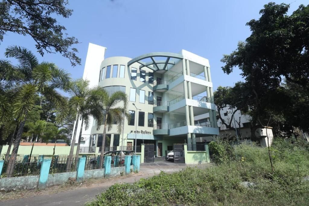 A multi-story building with a curved facade, a gated entrance, and a parking area.