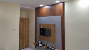 A modern bathroom with a wooden vanity, a mounted TV, and a small shelf with toiletries. - The Pride Gitbitan (Asansol)