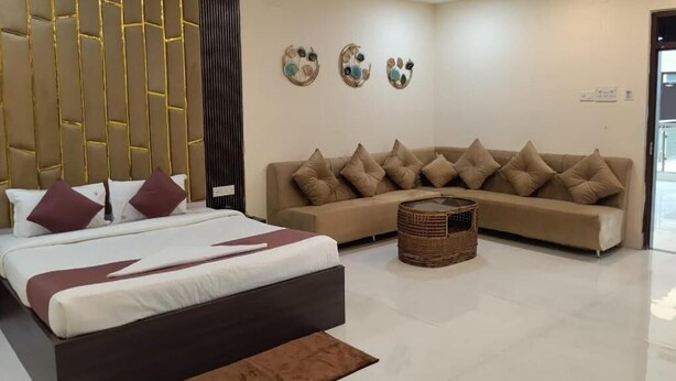 A modern hotel room with a large bed, a sofa, a small round coffee table, and a decorative wall panel. - The Pride Gitbitan (Asansol)