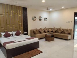 A modern hotel room with a large bed, a sofa, a small round coffee table, and a decorative wall panel.