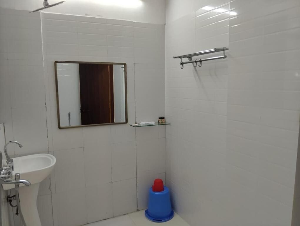 A bathroom with white tiled walls, a sink, a mirror, and a shower area.