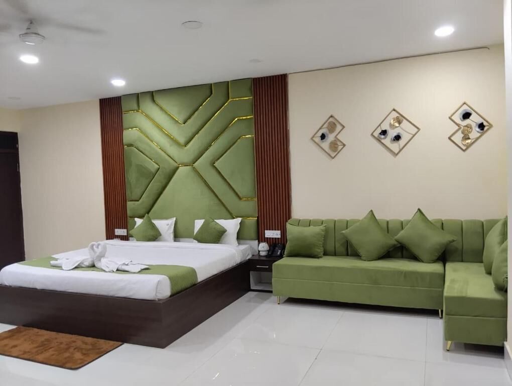 Quarto de hotel moderno com uma cama grande, um sofá verde e um painel decorativo na parede.
