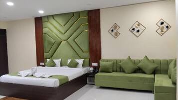 Quarto de hotel moderno com uma cama grande, um sofá verde e um painel decorativo na parede.