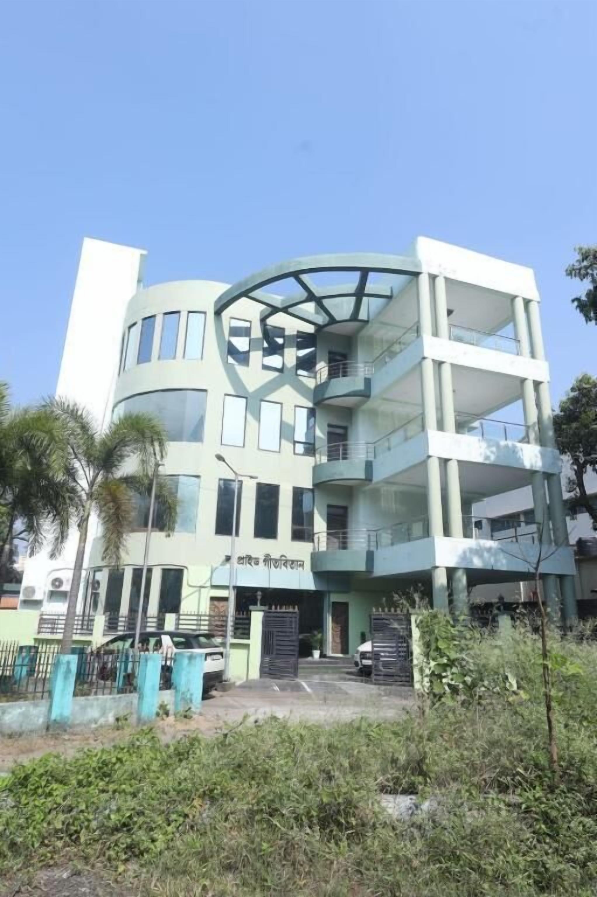 Un edificio de varios pisos con fachada de vidrio curva, entrada verde y un cartel con texto.