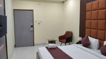 A hotel room with a bed, a chair, a small table, and a door.