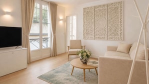 Ein modernes Wohnzimmer mit Flachbildfernseher, beiger Couch, rundem Couchtisch mit floralem Arrangement und einer dekorativen Wandverkleidung.