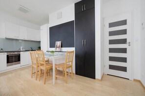 Cuina moderna amb armaris blancs, un frigorífic negre i una taula de dinar amb caires.