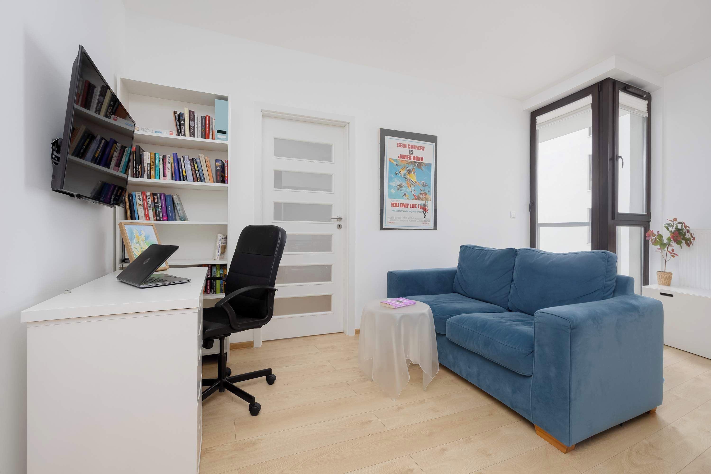 Ein Zimmer mit Schreibtisch, Stuhl, Bücherregal, blauem Sofa und einem Poster an der Wand.