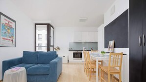 Ein modernes Wohnzimmer mit einem blauen Sofa, einem Esstisch mit Stühlen, einer Küchenzeile und einem schwarzen Kleiderschrank.