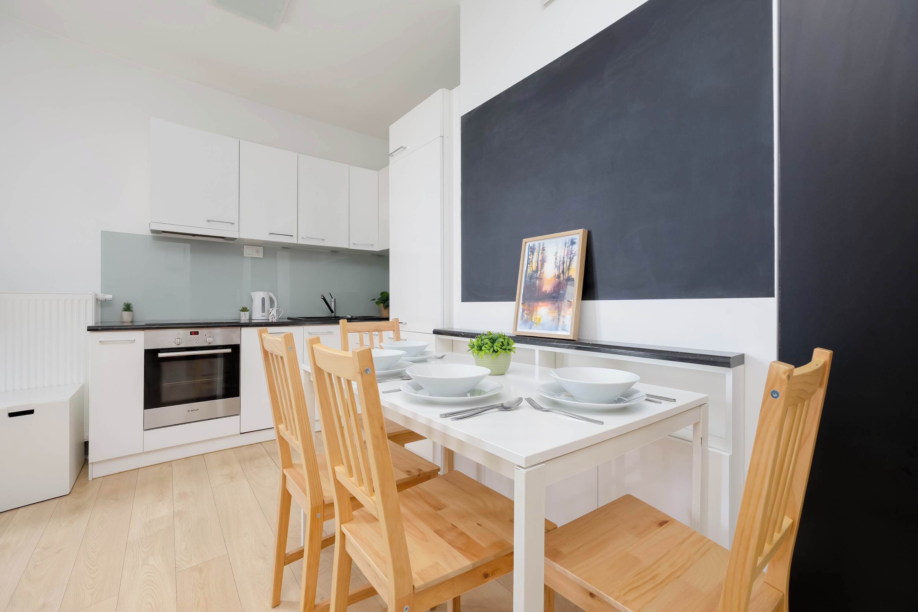 Une cuisine moderne avec des armoires blanches, un four encastré et une table à manger accompagnée de chaises.