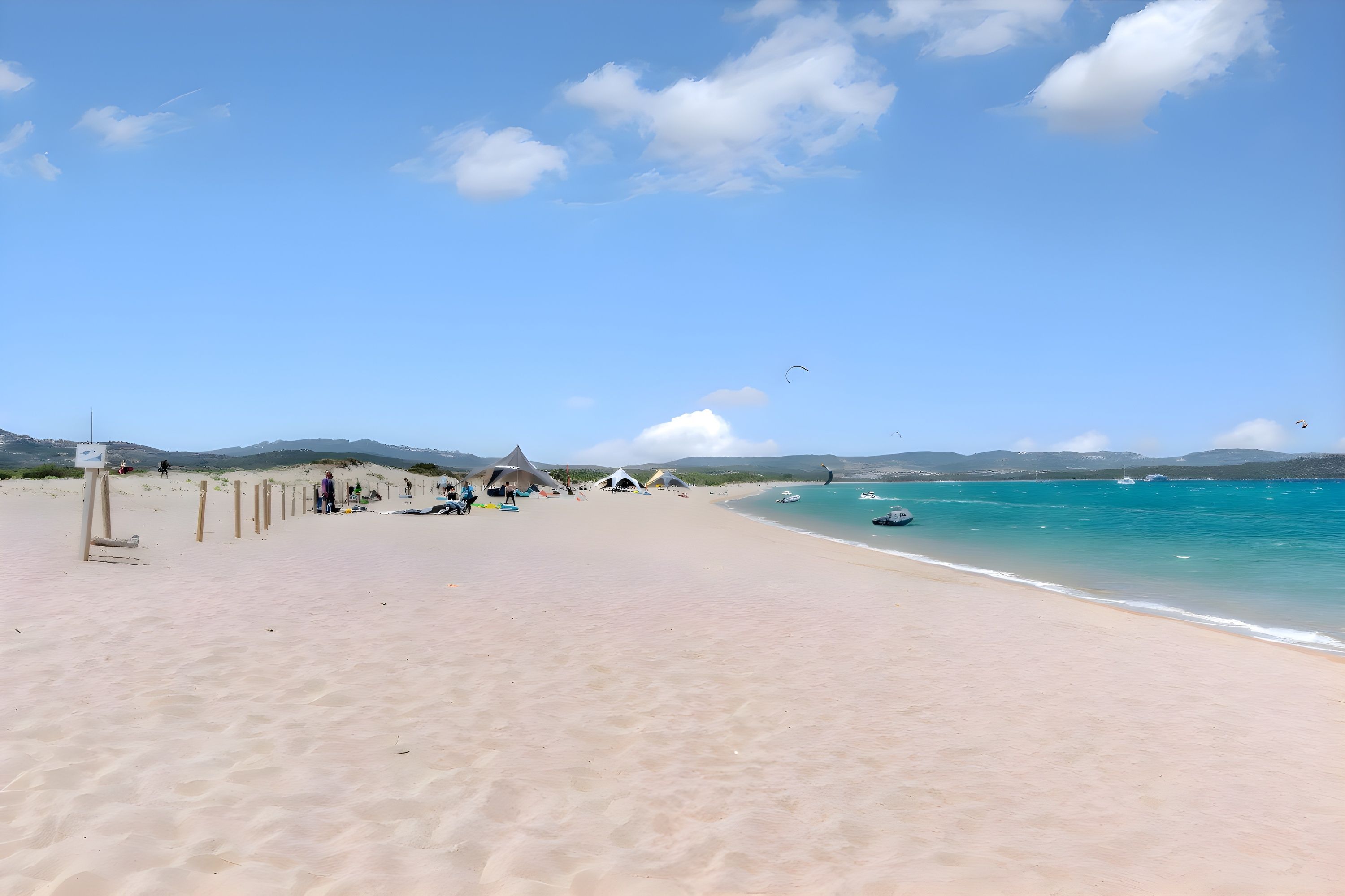 A beach with clear skies, a sandy shore, and a few tents in the distance.
