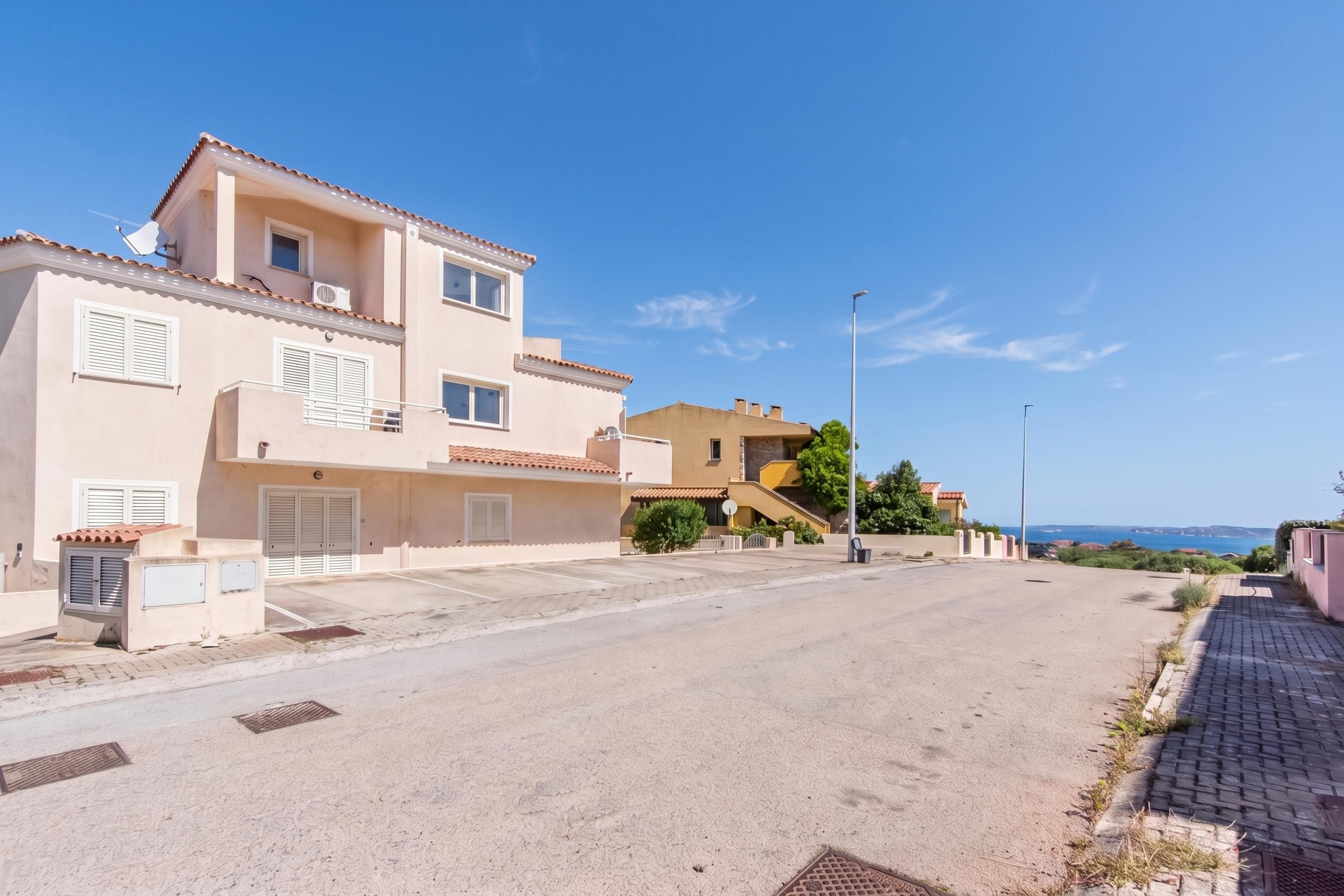 A residential street with houses, a clear sky, and a view of the sea.