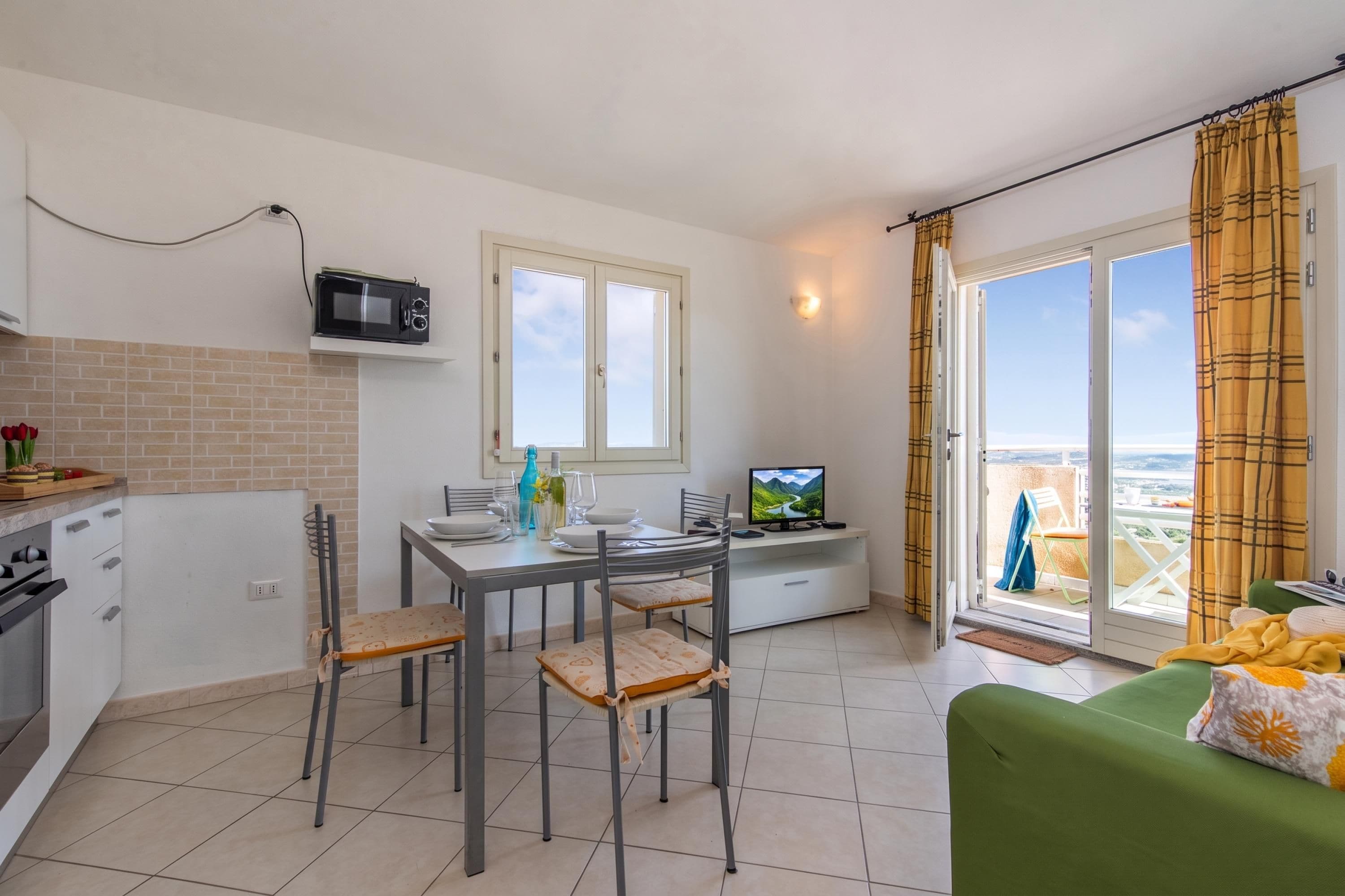 A compact living space with a kitchenette, dining area, and a balcony with a view.