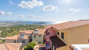 Una zona residencial costera con edificios de tejas color terracota, cielo despejado y vista distante al mar.