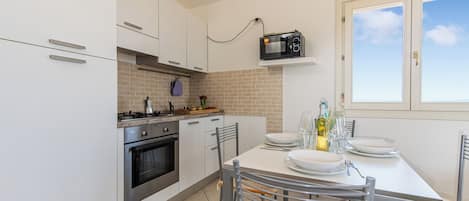 Una cocina con armarios blancos, microondas, estufa y una mesa de comedor con platos y vasos.