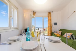 A dining area with a table set for two, a green sofa, and a view of the sea. - Elicriso (Tempio Pausania)